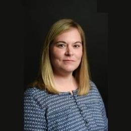 Lady with dark blonde hair wearing blue paisley button up top in front of black background