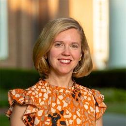 Lady with short blonde hair wearing multi colored orange and gold top