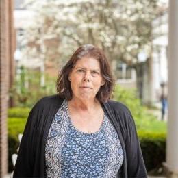 Lady with dark hair wearing multi patterned top and black cardigan standing on porch