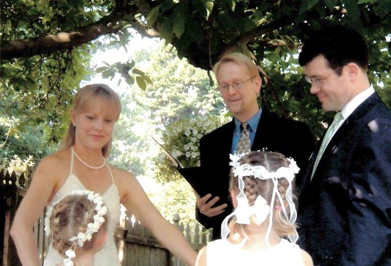 A bride, groom and officiant look at two small girls taking part int the wedding ceremony.