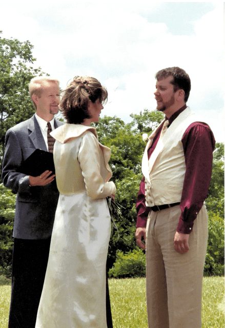 A groop, bride and wedding officiant stand in a field during a marriage ceremony. 